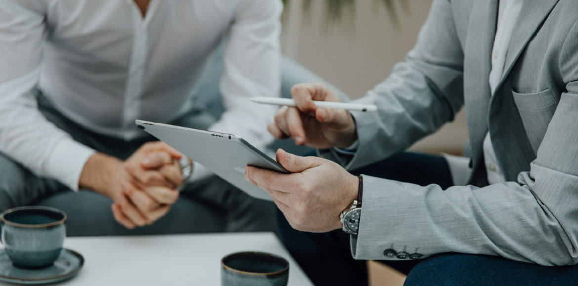 two men sitting at a table with a tablet